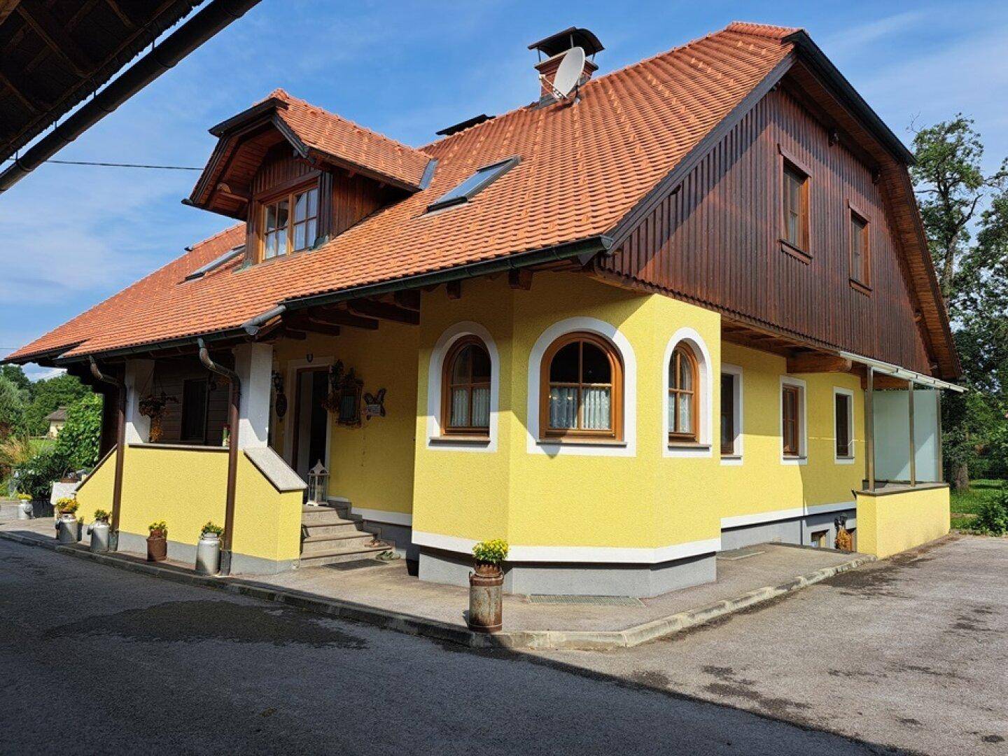 Traditionelles Haus mit gelber Fassade, Holzelementen und rotem Ziegeldach unter blauem Himmel.