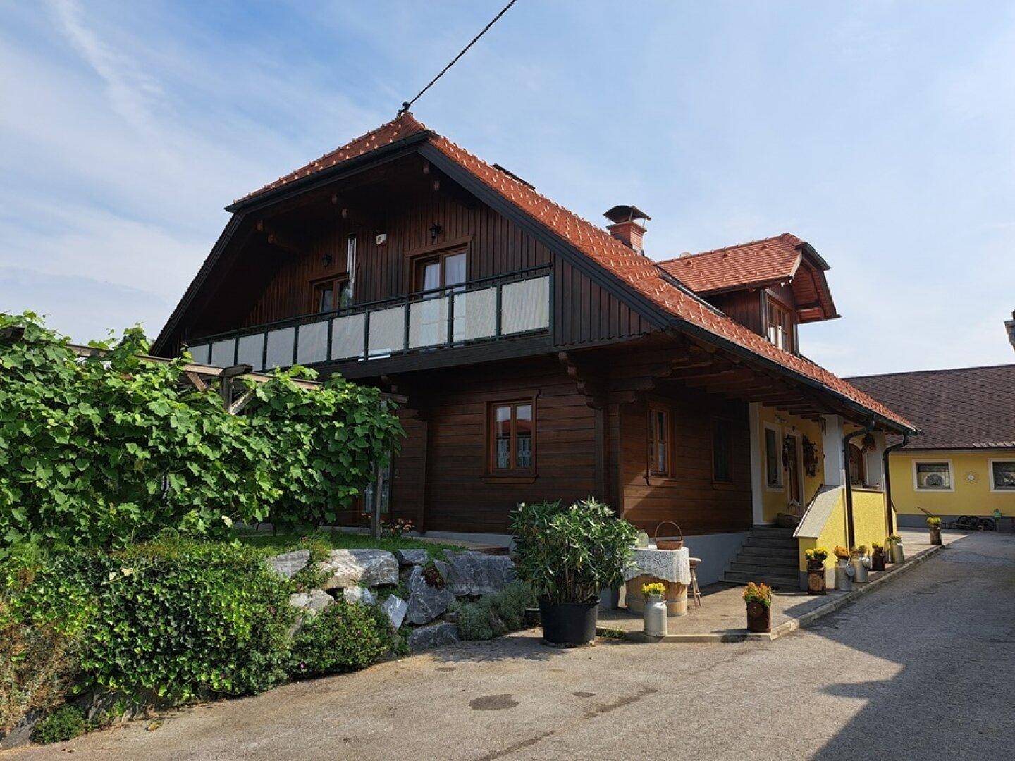 Seitenansicht des Hauses mit Holzbalkon, üppigem Grün und traditioneller Architektur.