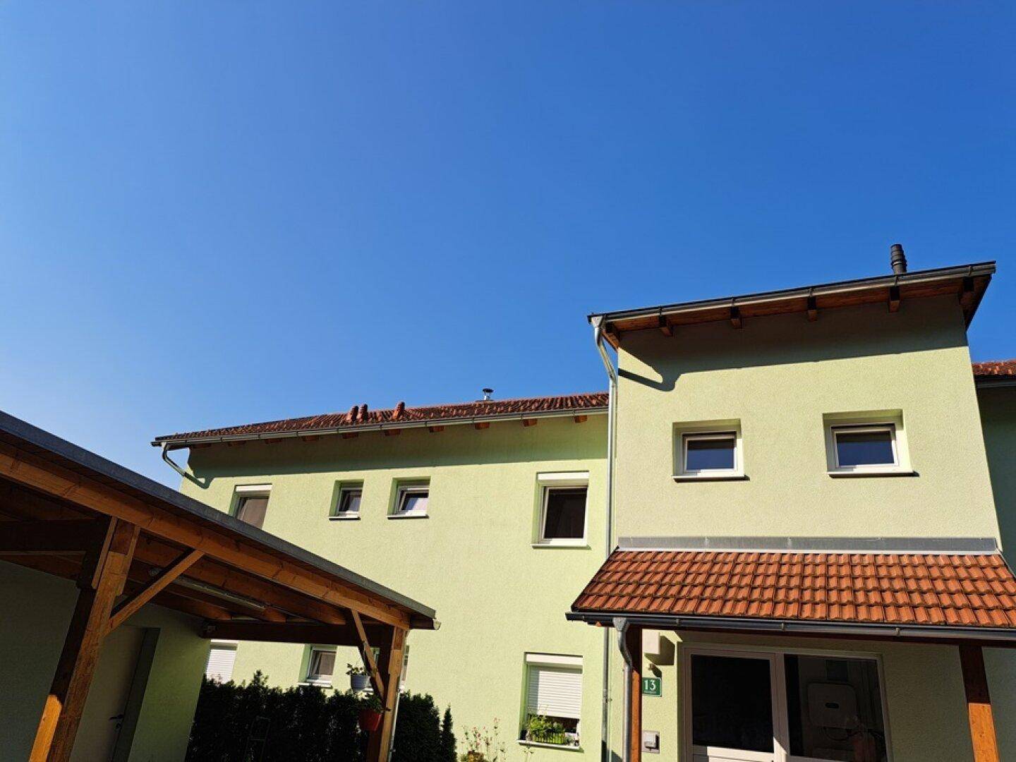 Wohngebäude mit hellgrüner Fassade, Satteldach und einem Holzcarport im Vordergrund.