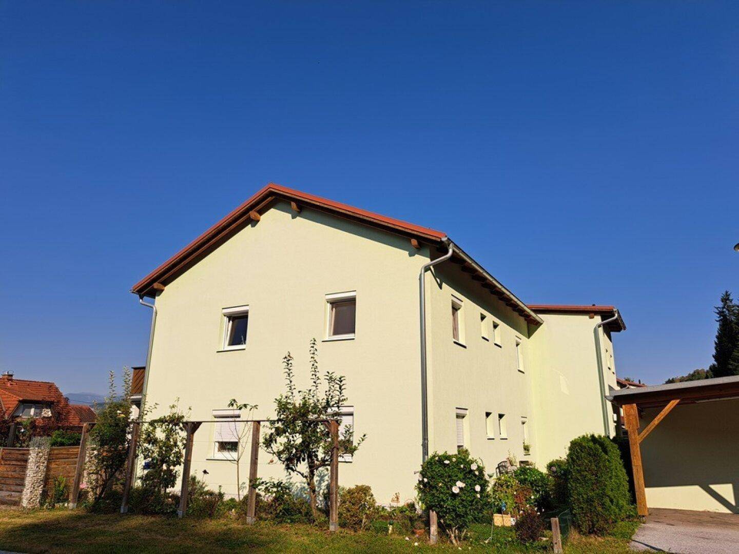 Freistehendes Haus mit hellgrüner Fassade und Satteldach, umgeben von Bäumen und Garten.