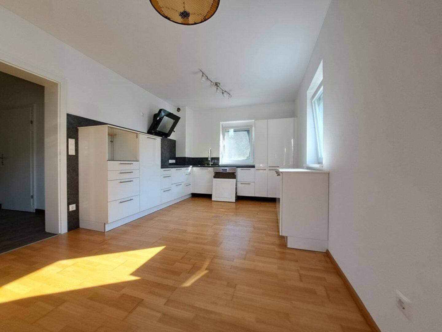 Helle Küche mit weißen Schränken, Holzboden und Blick nach draußen durch das Fenster.