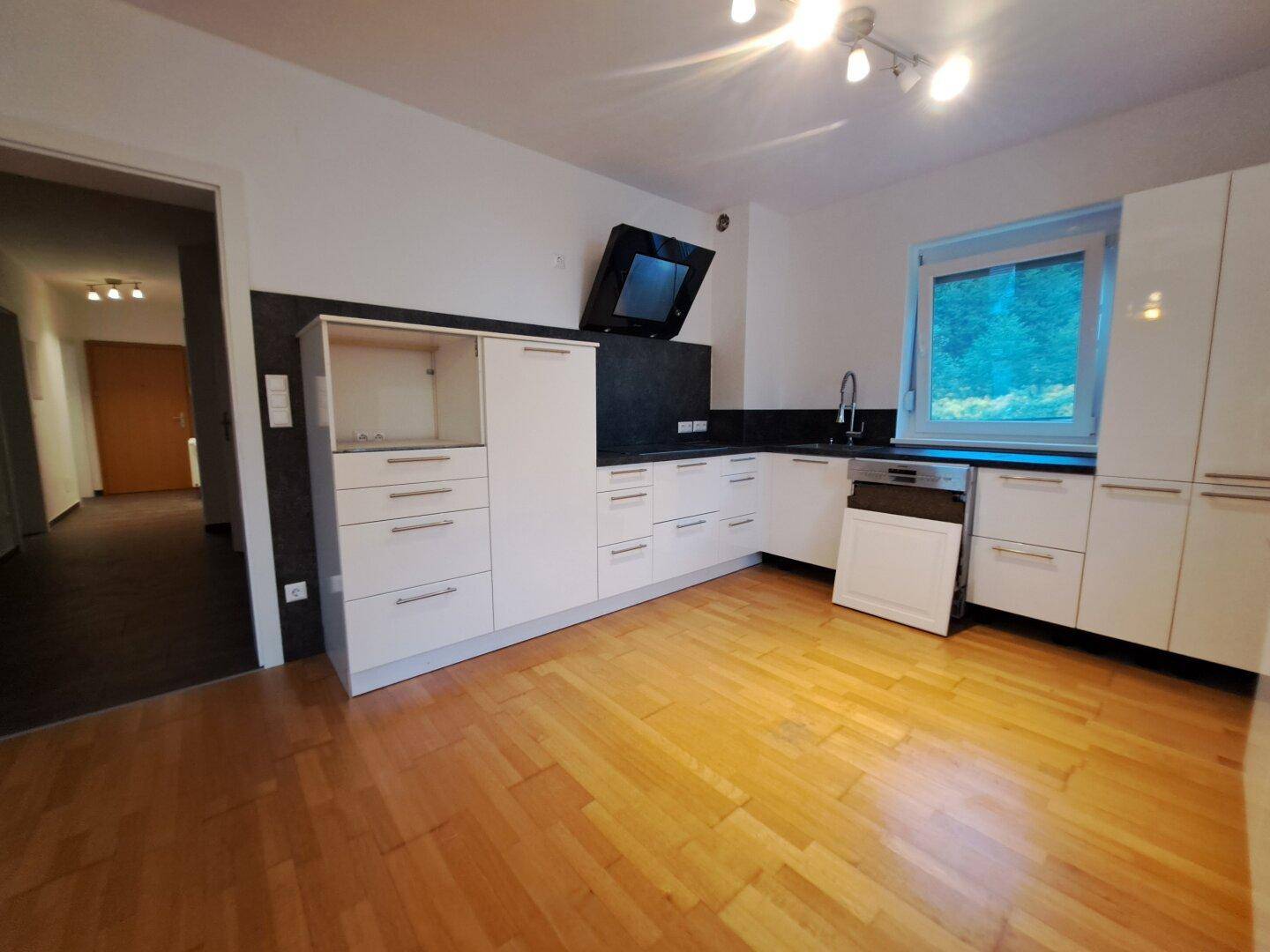 Moderne Einbauküche in Weiß mit dunkler Arbeitsplatte und Holzboden in einem hellen Raum.