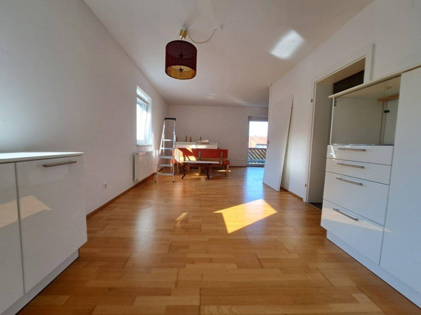 Heller Wohnbereich mit Holzboden, großen Fenstern und Zugang zu einem Balkon.
