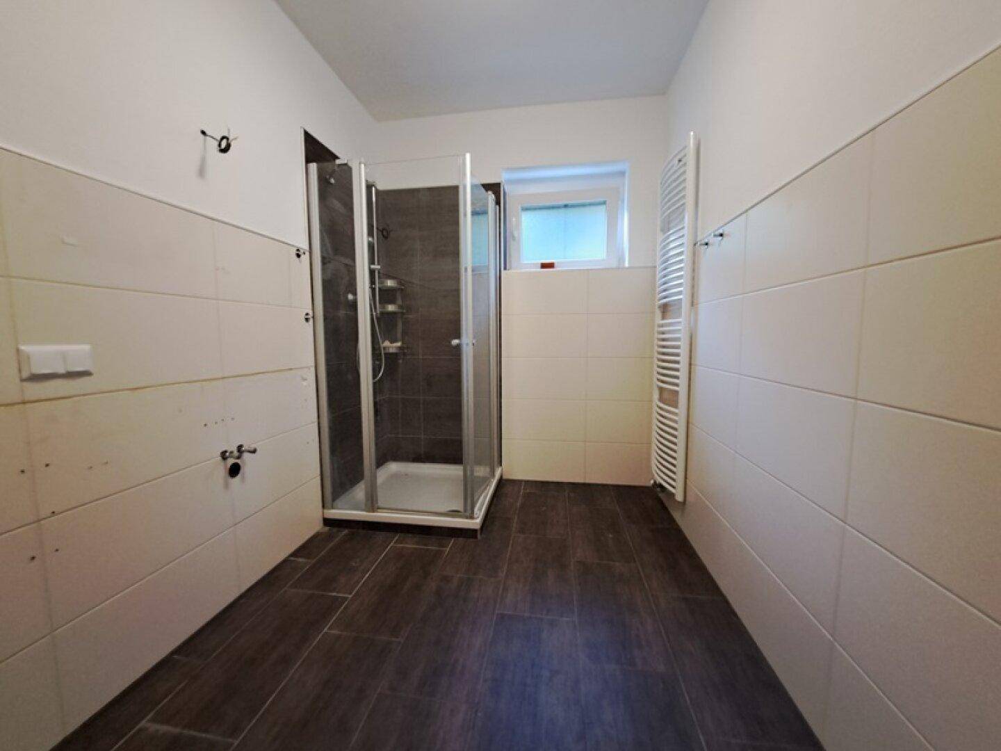 Modernes Badezimmer mit Duschkabine, dunklen Bodenfliesen und beheiztem Handtuchhalter.