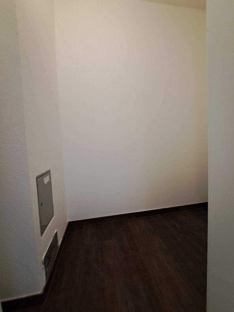 Leerer Abstellraum mit dunklen Fliesen und weißen Wänden, ideal für zusätzlichen Stauraum.