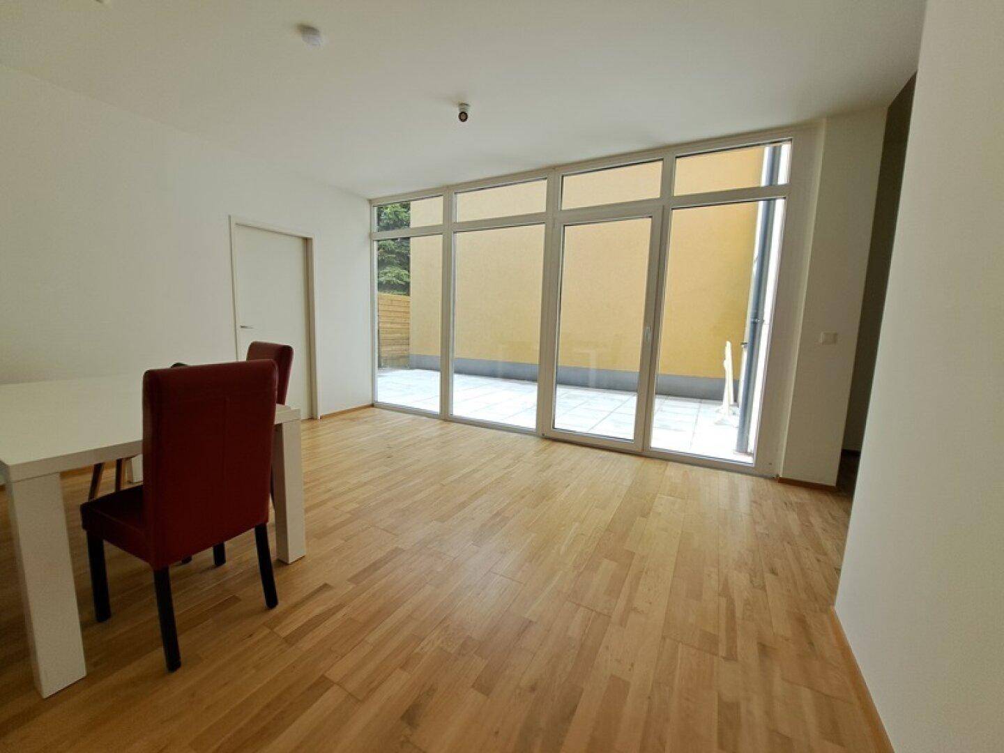 Heller Essbereich mit Holzboden und großen Fenstern, die Zugang zur Außenterrasse bieten.