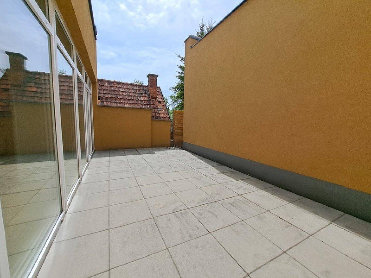 Geräumige, geflieste Terrasse neben dem Gebäude, ideal für entspannte Stunden im Freien.