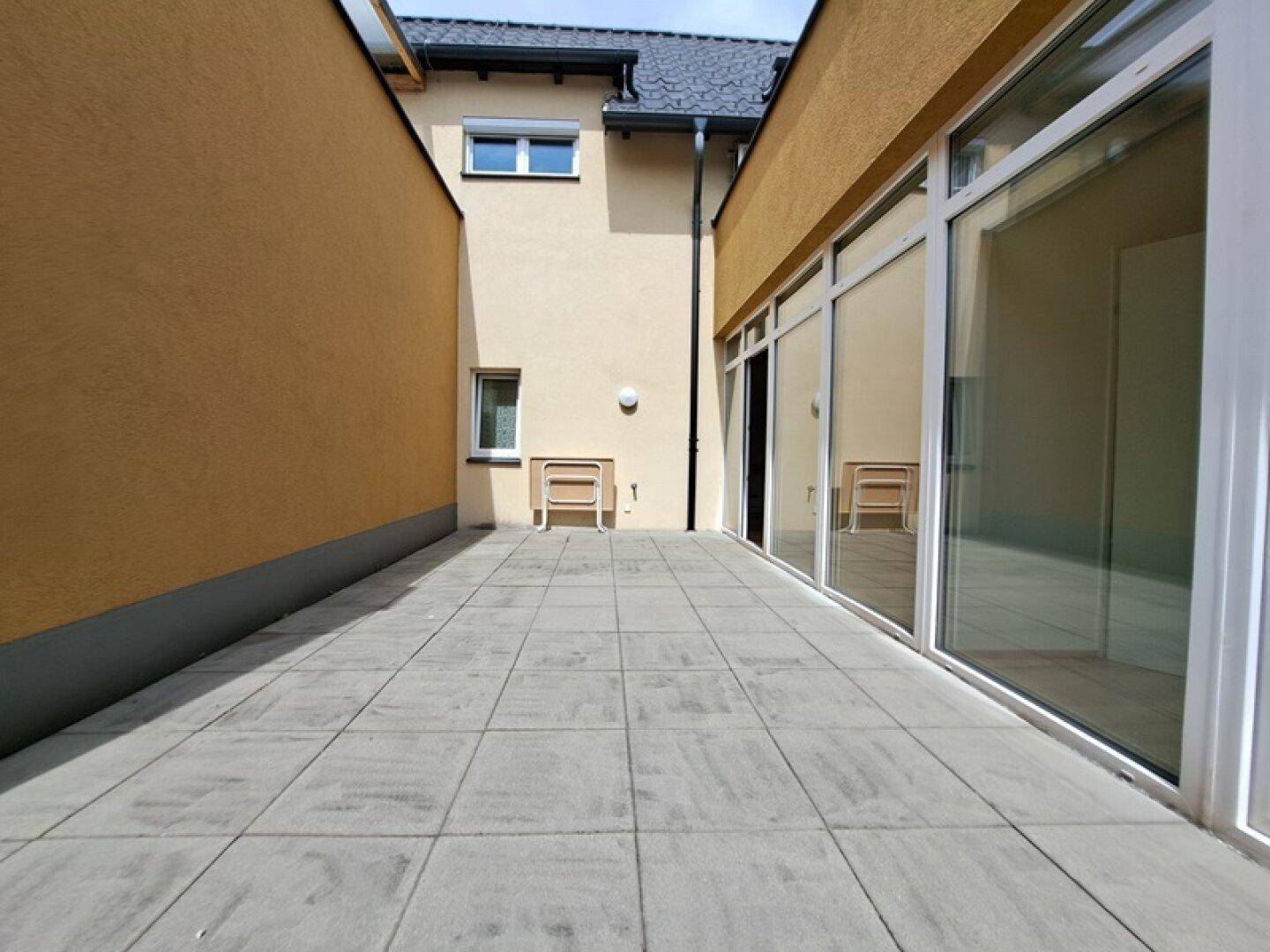 Lange, geflieste Terrasse zwischen zwei Gebäudeteilen, bietet Platz für Outdoor-Aktivitäten.