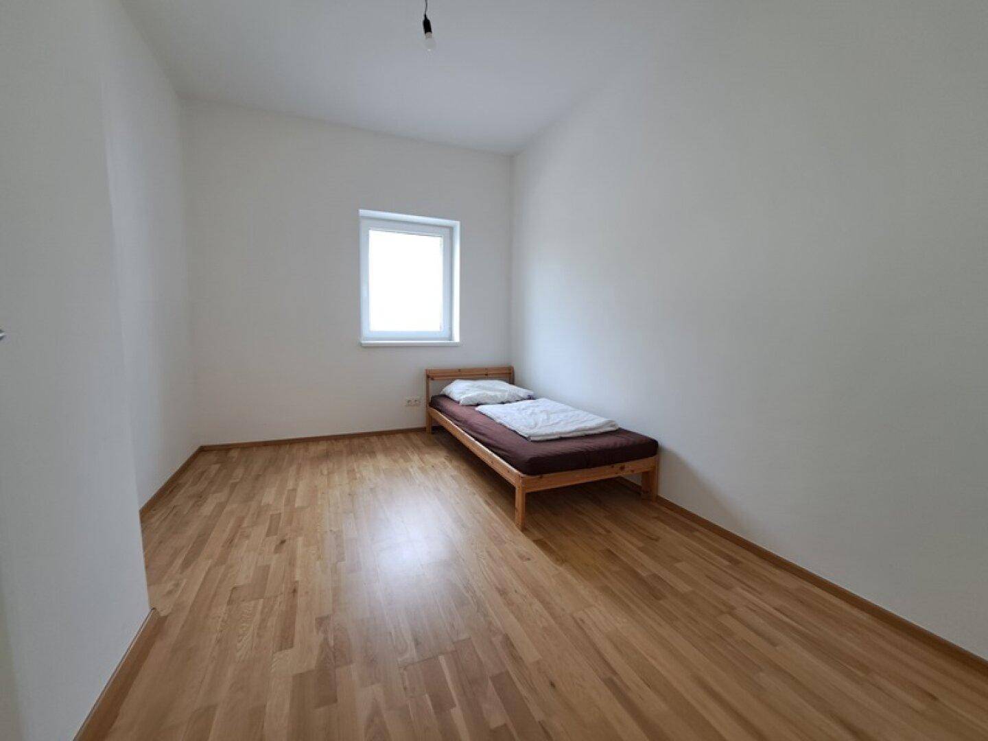 Einfaches Schlafzimmer mit Einzelbett und Holzboden, bietet eine ruhige Rückzugsmöglichkeit.