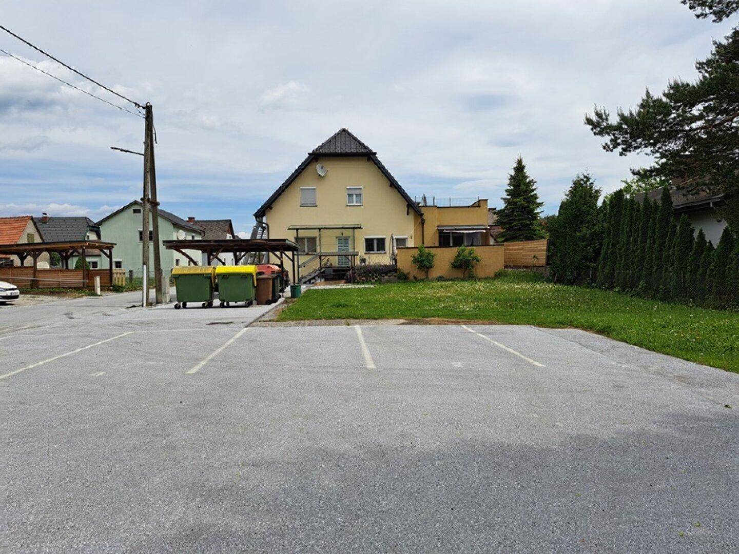 Rückansicht des Hauses mit Rasenfläche und Parkplätzen im Vordergrund.
