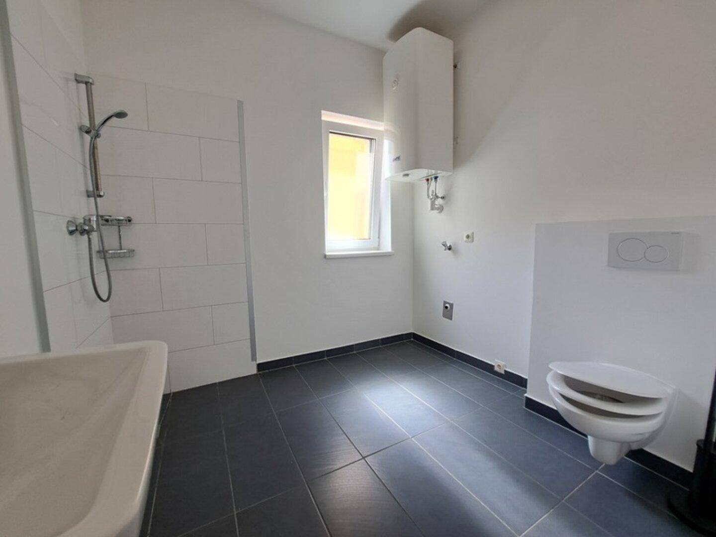 Helles Badezimmer mit Dusche, wandhängender Toilette und Fenster für natürliche Belüftung.