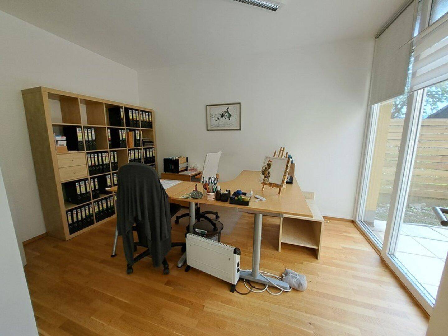 Geräumiges Büro mit Schreibtisch, Regalen und großen Fenstern mit Zugang zur Terrasse.