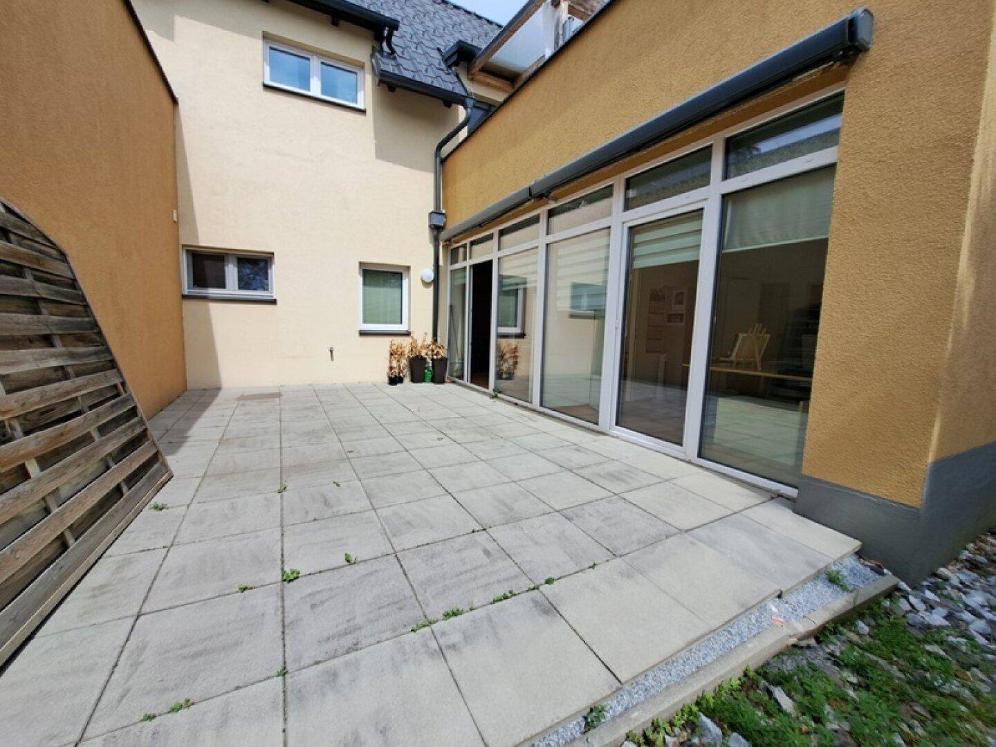 Geflieste Terrasse neben dem Gebäude, umgeben von einer Holzwand, ideal für Privatsphäre.
