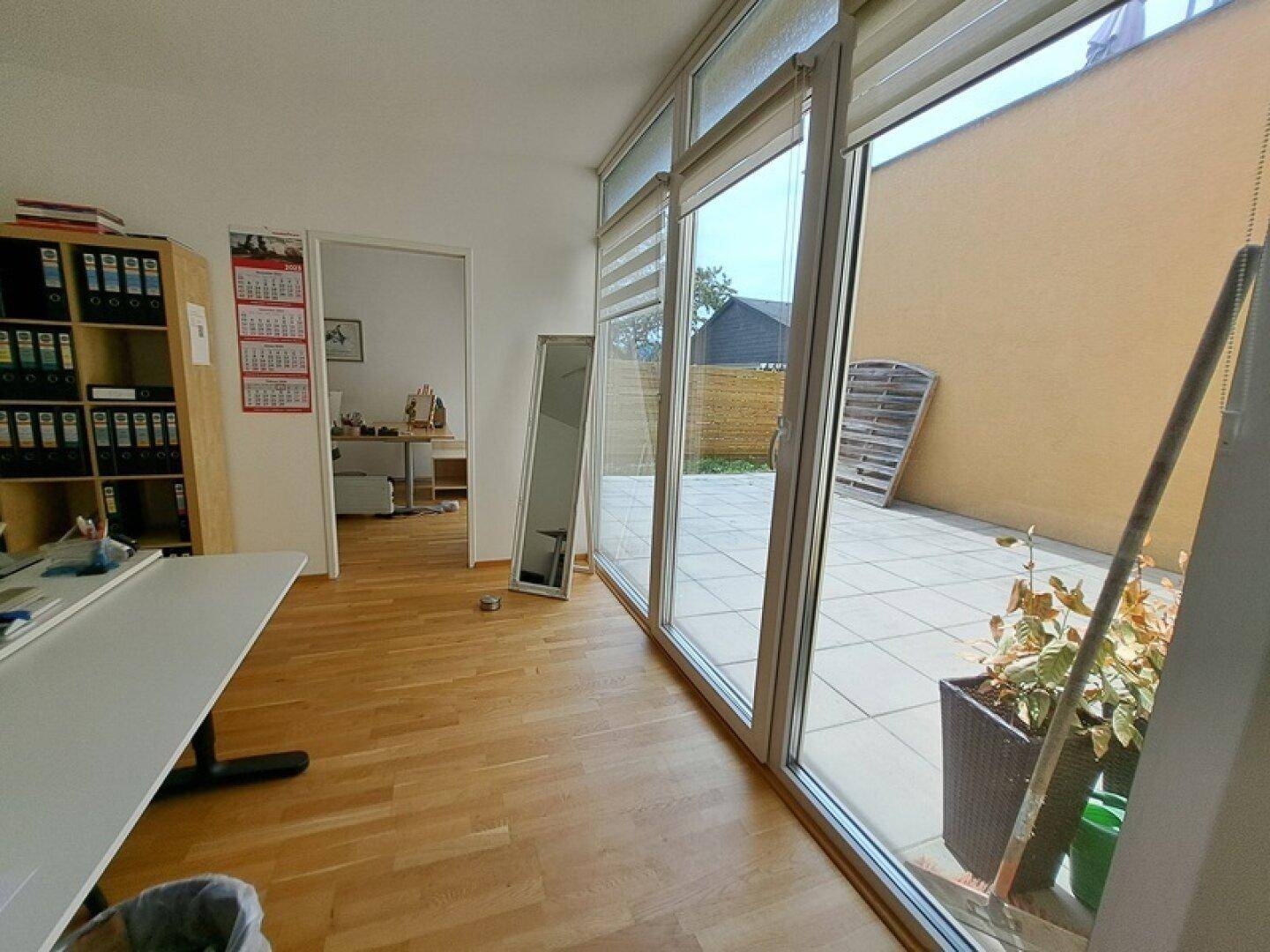 Helles Büro mit Schreibtisch und großer Fensterfront, die Zugang zu einer Außenterrasse bietet.