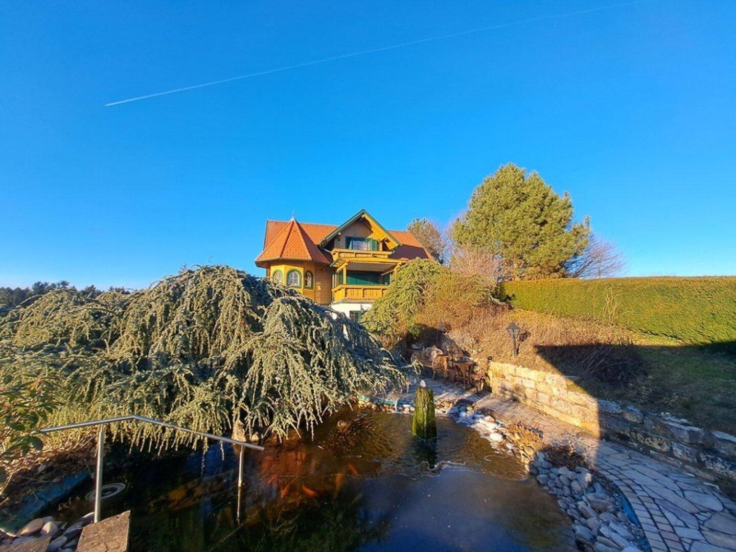 Traditionelles Holzhaus mit Teich und üppiger Bepflanzung im Vorgartenbereich.