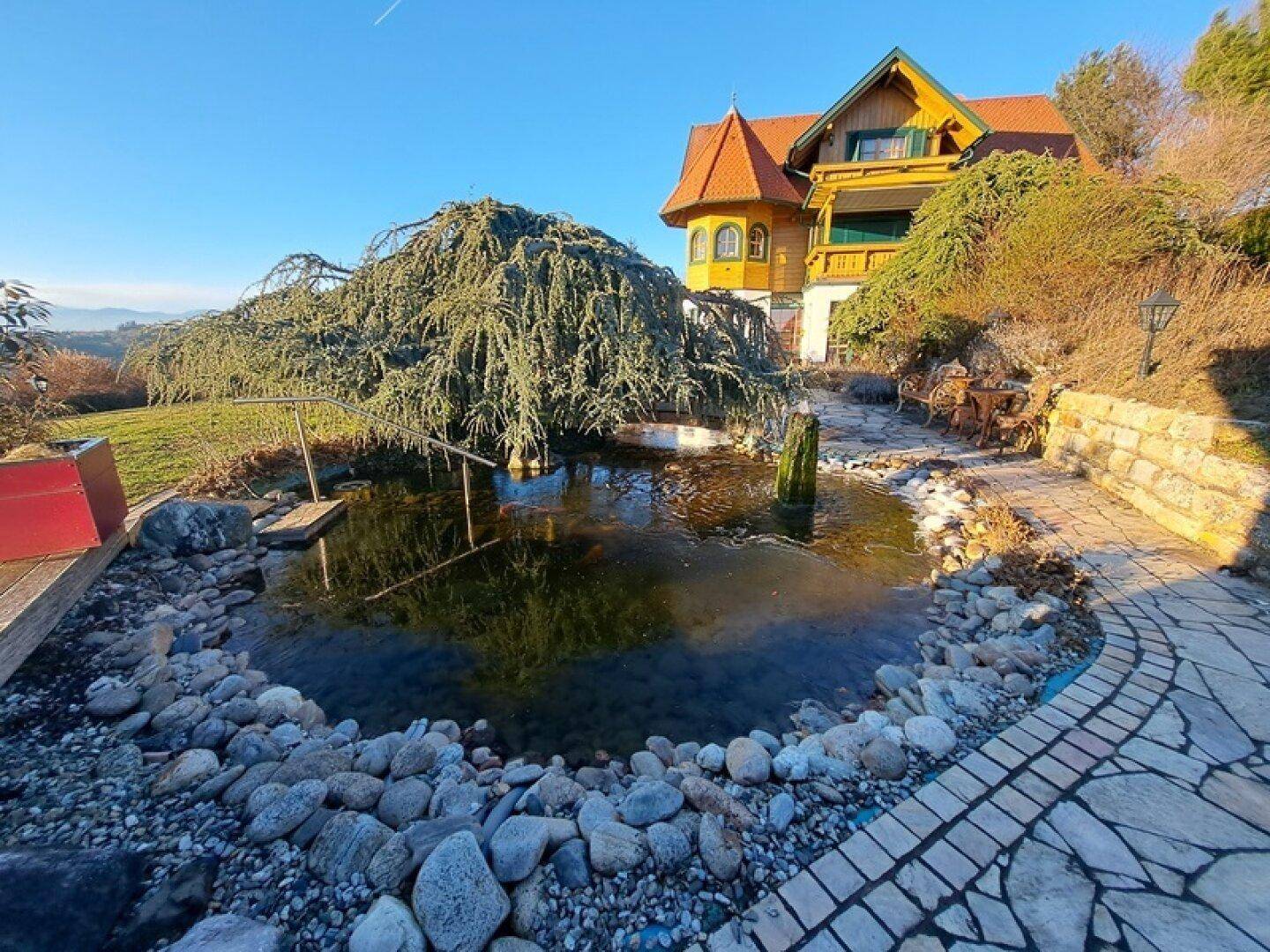 Idyllischer Gartenteich mit Steinen und üppiger Bepflanzung vor dem Holzhaus.