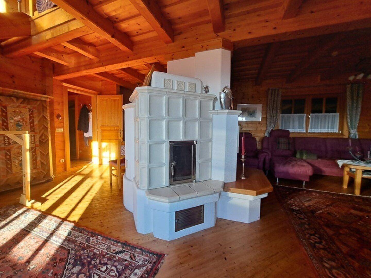 Geräumiges Wohnzimmer mit traditionellem Kachelofen, Holzboden und Holzbalkendecke.