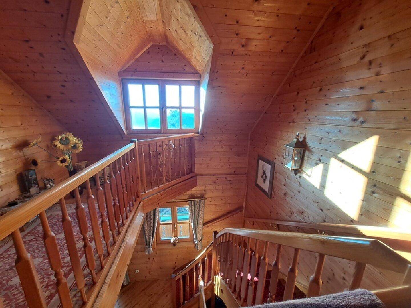 Holztreppenhaus mit mehreren Etagen und Fenstern, das viel Licht hereinlässt.