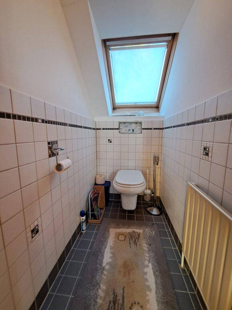 Modernes WC mit Dachfenster, Fliesen an den Wänden und dunklem Fliesenboden.
