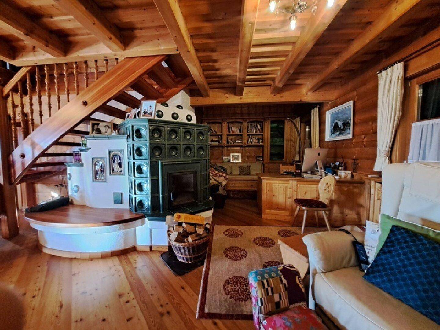 Wohnbereich mit grünem Kachelofen, Holztreppe und integriertem Arbeitsplatz.