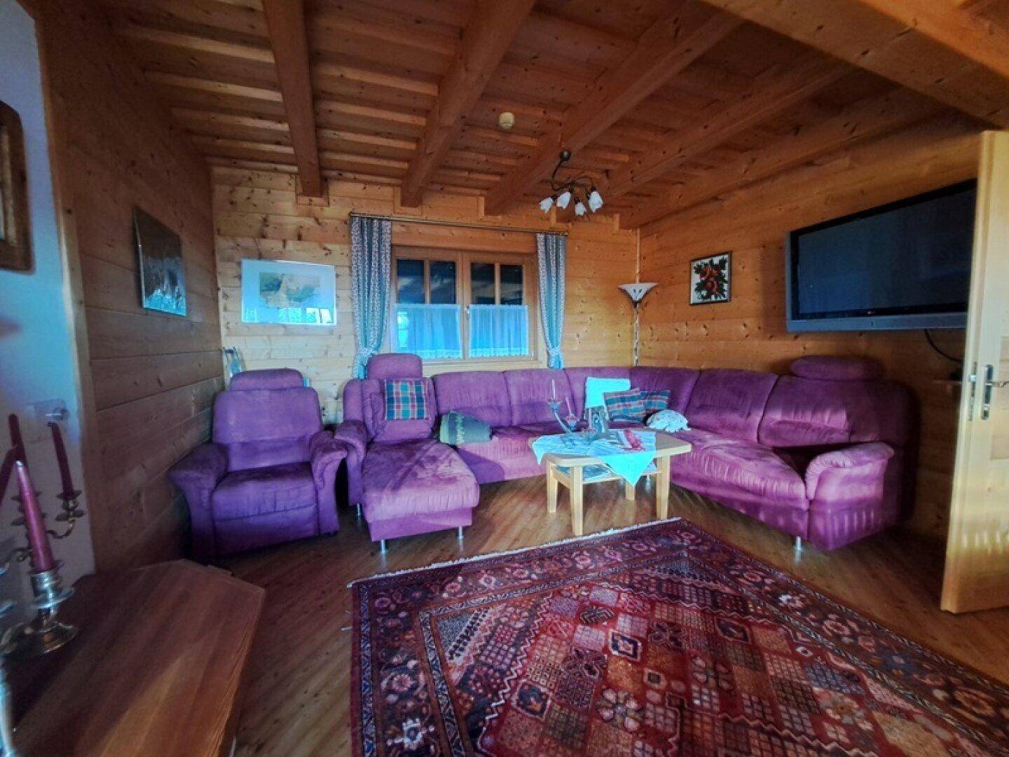Gemütliches Wohnzimmer mit violetter Sofagarnitur, Holzwänden und Teppichboden.