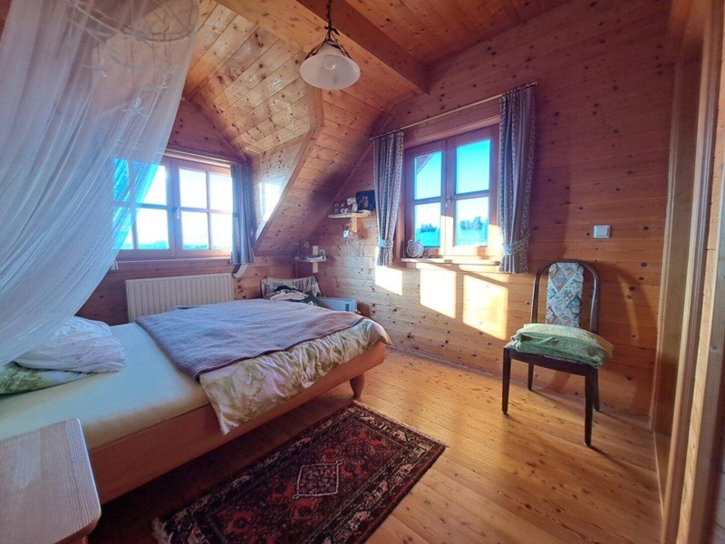 Helles Schlafzimmer mit Holzwänden, Holzboden und Fenstern mit Blick ins Grüne.