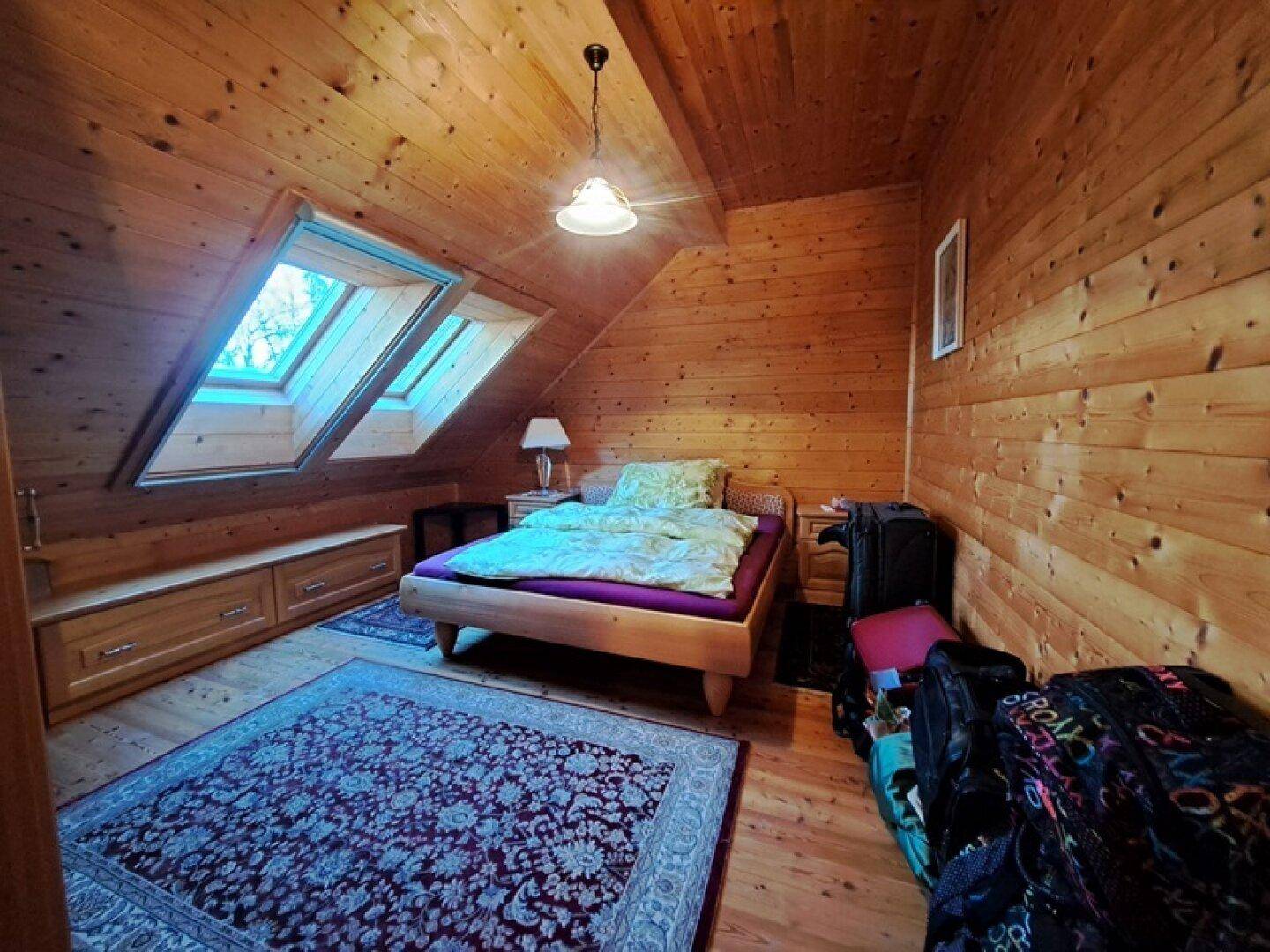 Gemütliches Schlafzimmer mit Holzwänden, Holzboden und zwei Dachfenstern.