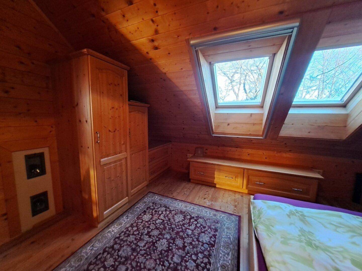 Schlafzimmer mit Holzwänden, Holzboden, Dachfenstern und Einbauschränken.