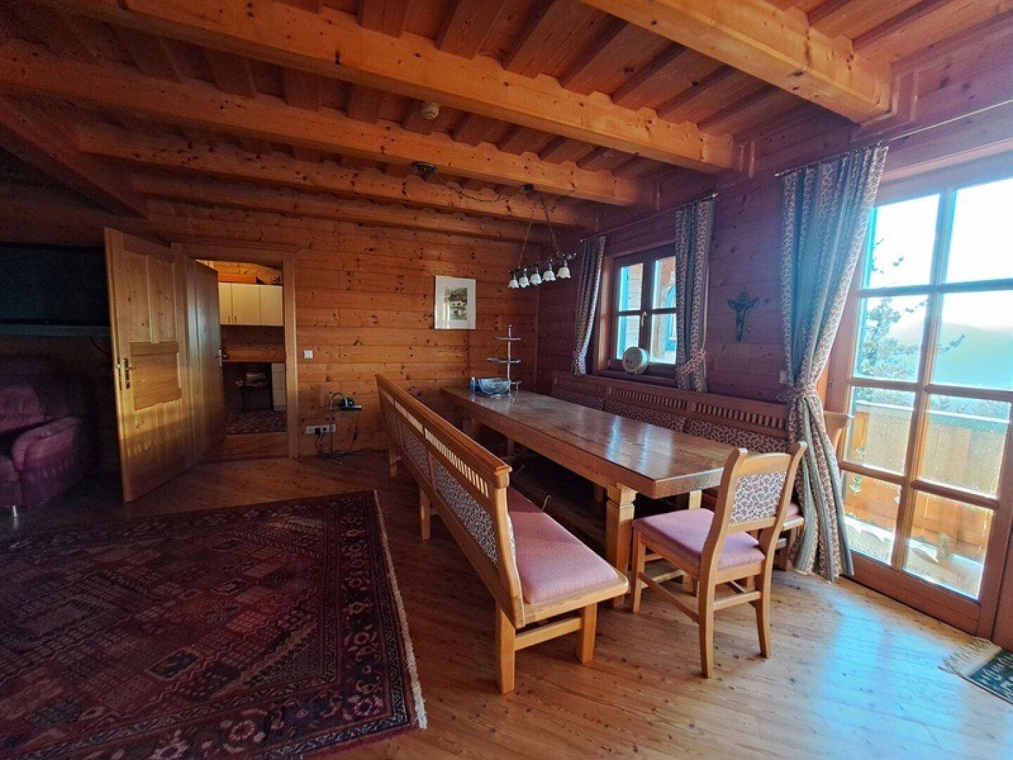Rustikaler Essbereich mit Holztisch und Bänken, Holzboden und Zugang zum Balkon.