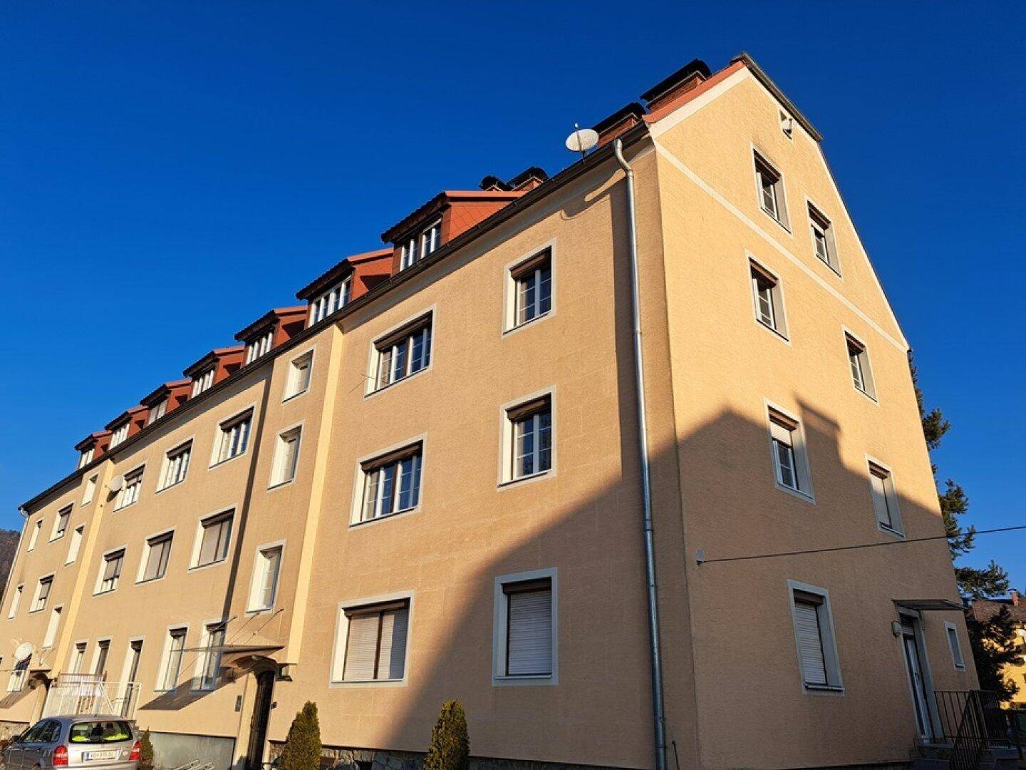 Mehrfamilienhaus mit gelber Fassade und vielen Fenstern unter blauem Himmel.