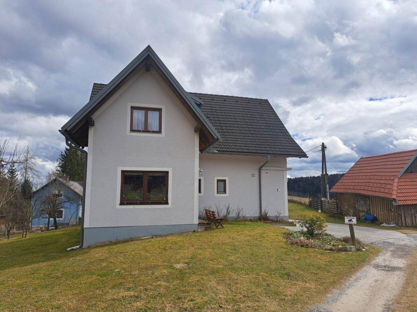 Seitenansicht des Hauses mit gepflegtem Rasen und Blick auf die umliegende hügelige Landschaft.