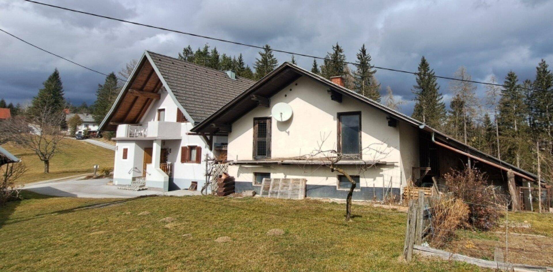 Das Haus liegt eingebettet in eine ländliche Umgebung mit viel Grün und Wald im Hintergrund.