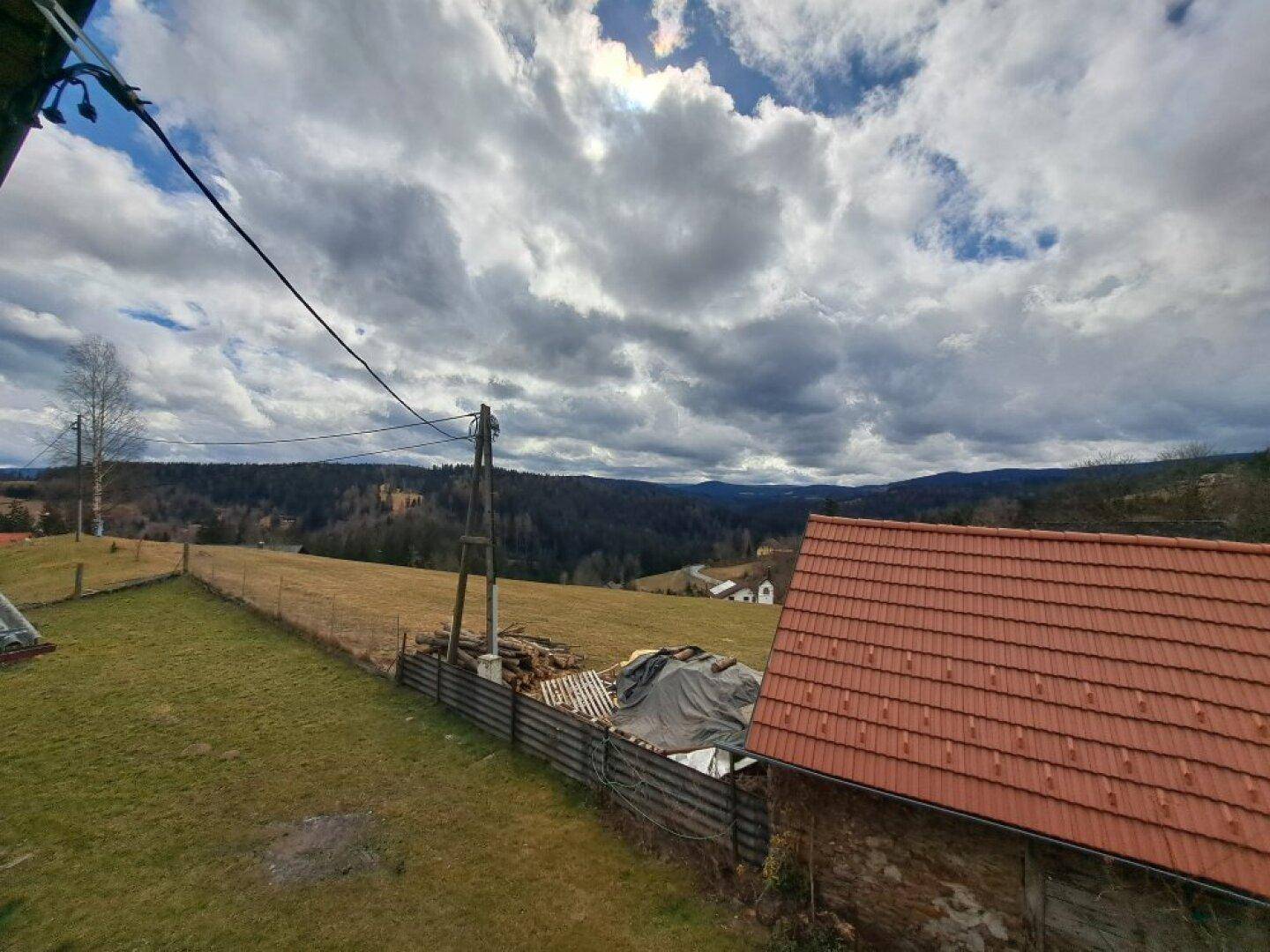Panoramablick über die hügelige Landschaft mit Wäldern und einem roten Dach im Vordergrund.