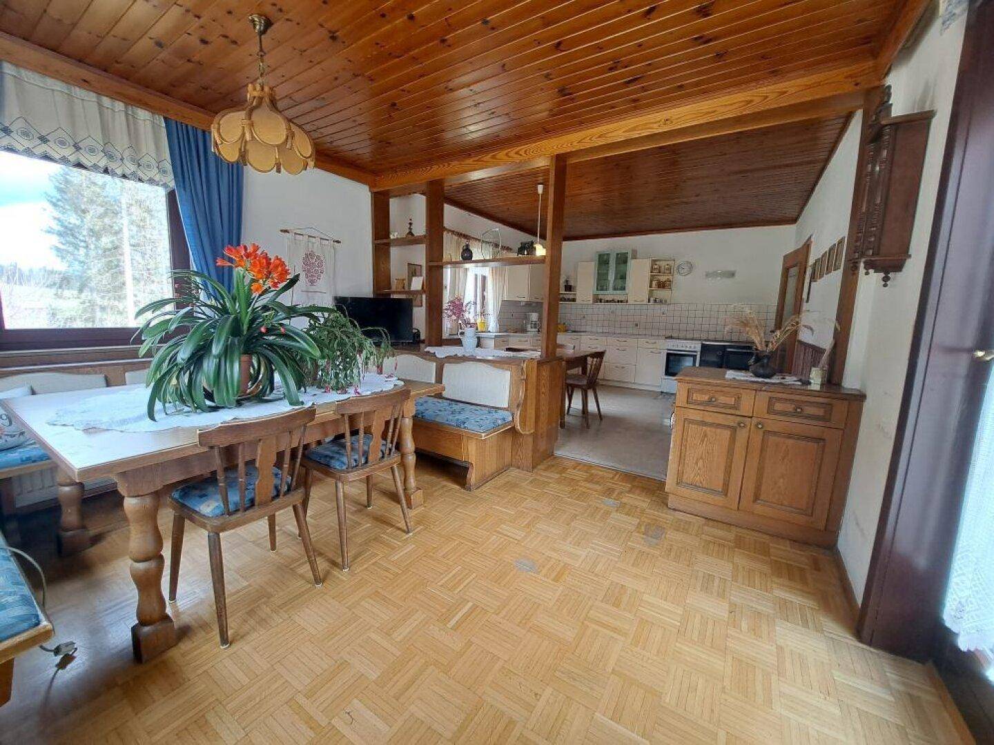 Gemütlicher Wohn-Essbereich mit Holzbalken, Parkettboden und Blick ins Grüne.