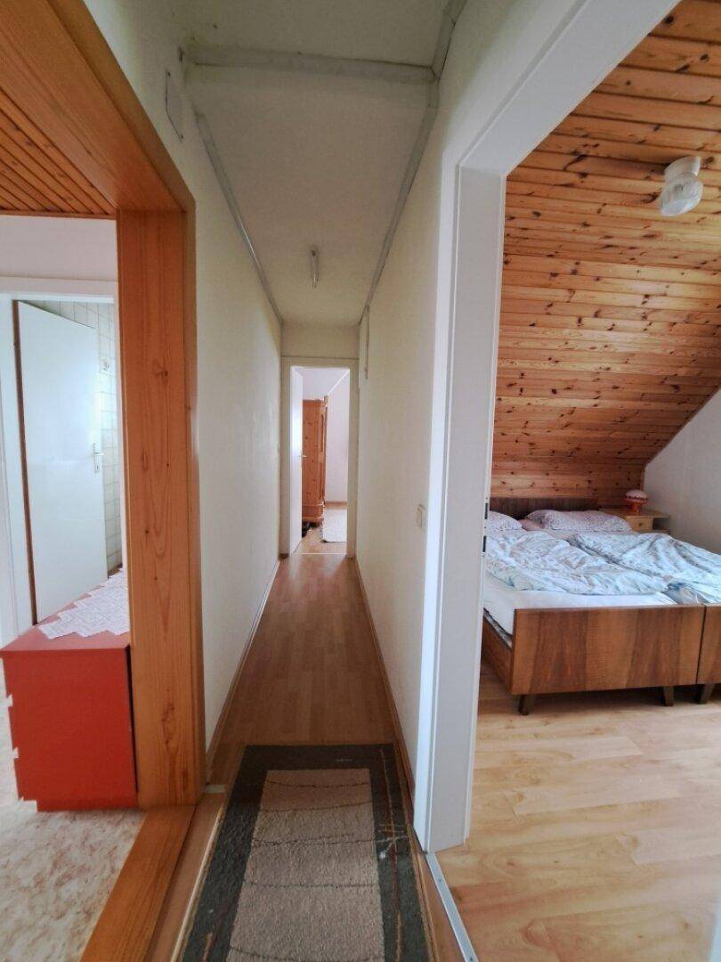 Heller Flur mit Holzfußboden und Blick in ein Schlafzimmer mit Holzverkleidung.