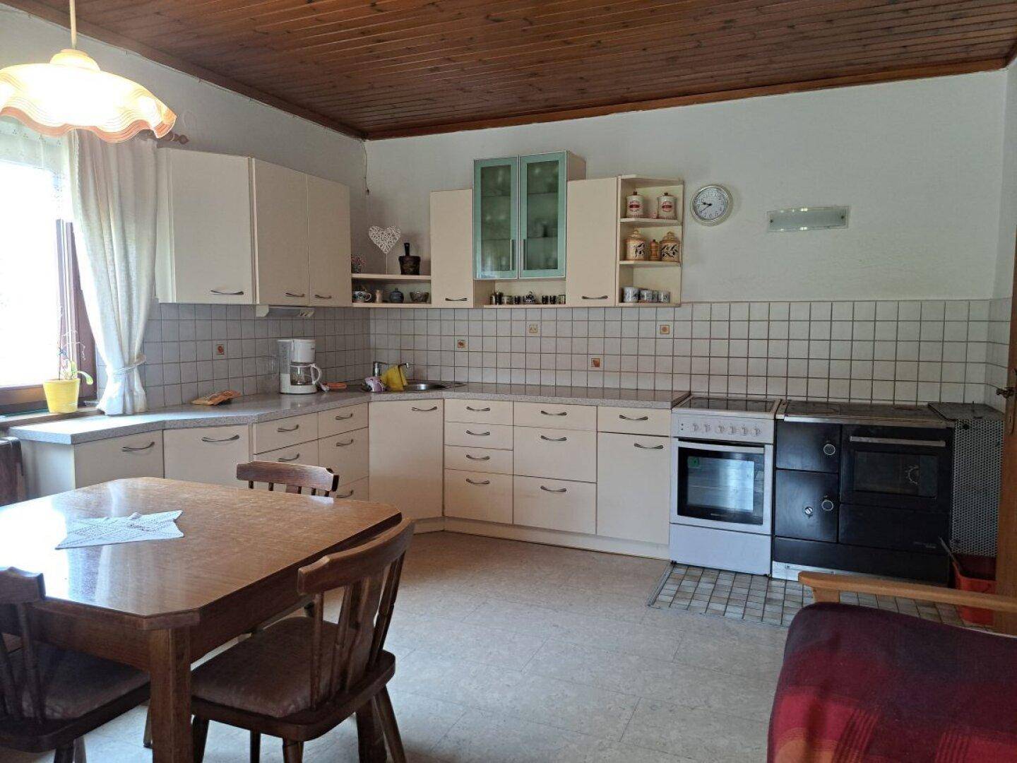 Funktionale Küche mit weißen Schränken, Fliesenrückwand und traditionellem Holzofen.