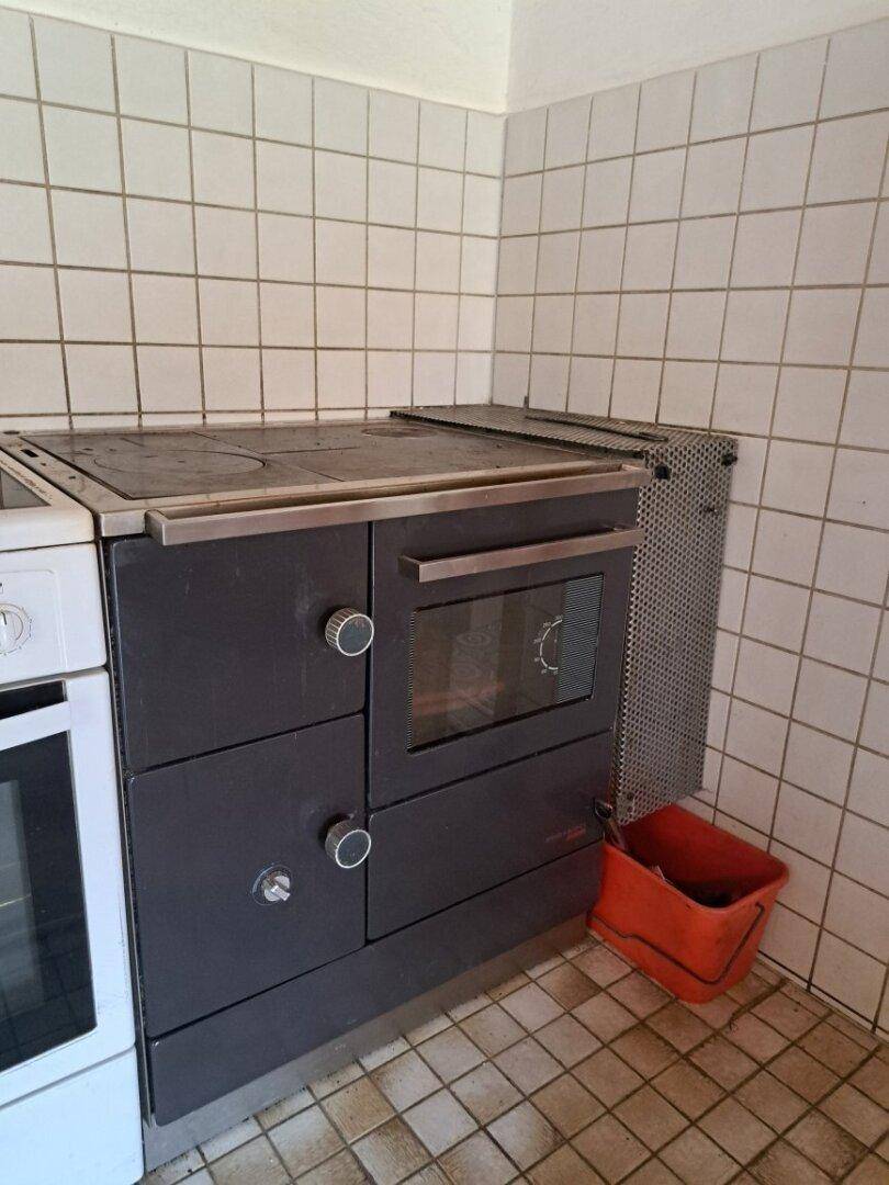 Detailansicht eines traditionellen Holzofens in der Küche mit Fliesenwand.