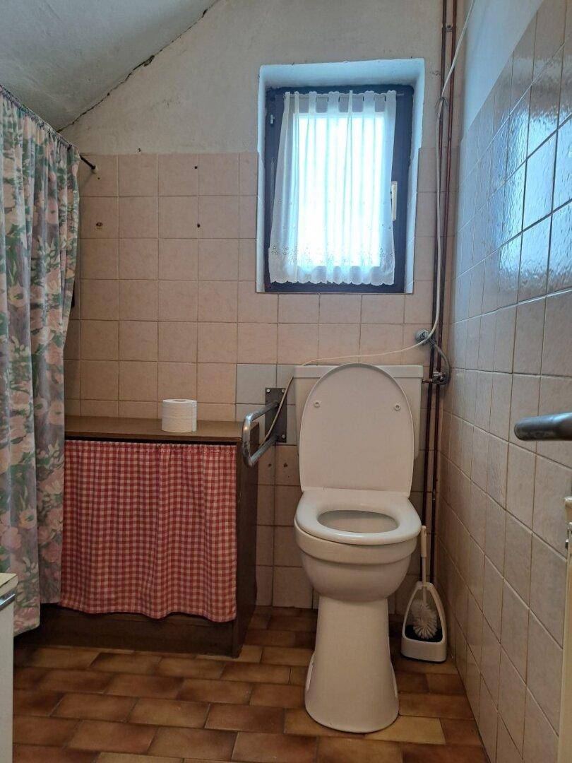 Einfaches WC mit Fenster, Toilette und Haltegriffen, funktional eingerichtet.