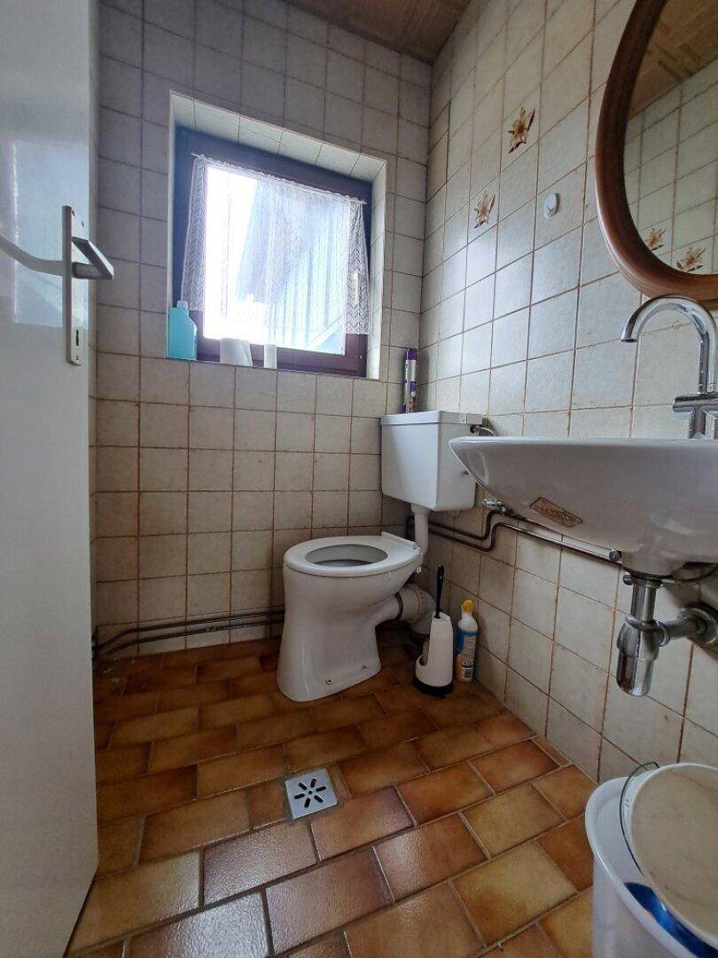 Kleines WC mit Fliesenboden, Waschbecken und Fenster, einfach und funktional.