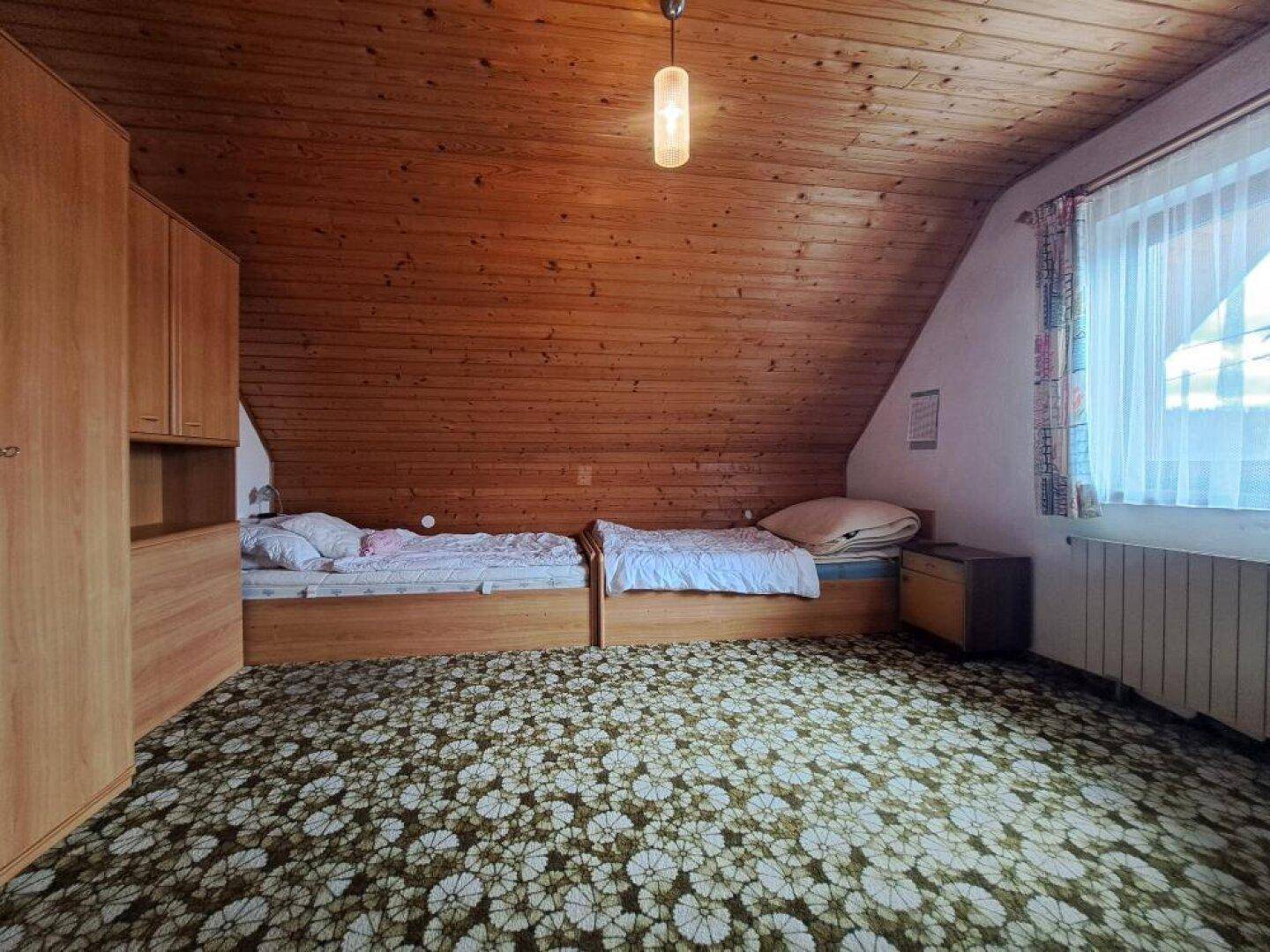 Schlafzimmer mit zwei Einzelbetten, Holzdecke und gemustertem Teppichboden.