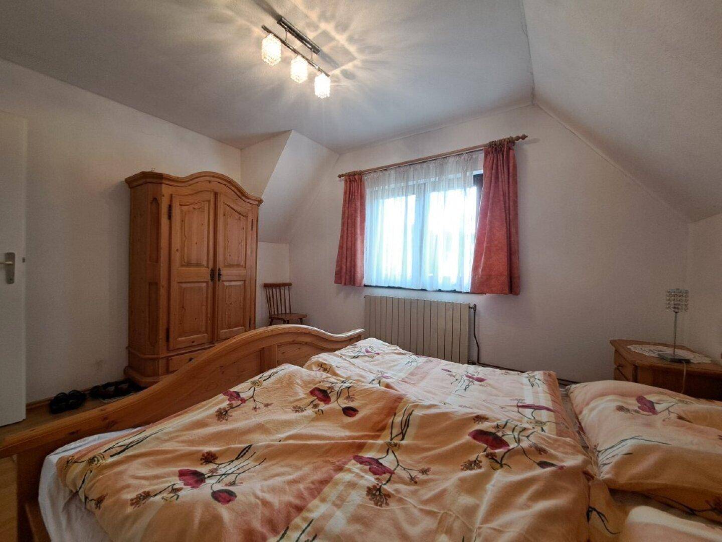 Schlafzimmer mit Holzbett, Kleiderschrank und Fenster, das viel Tageslicht hereinlässt.