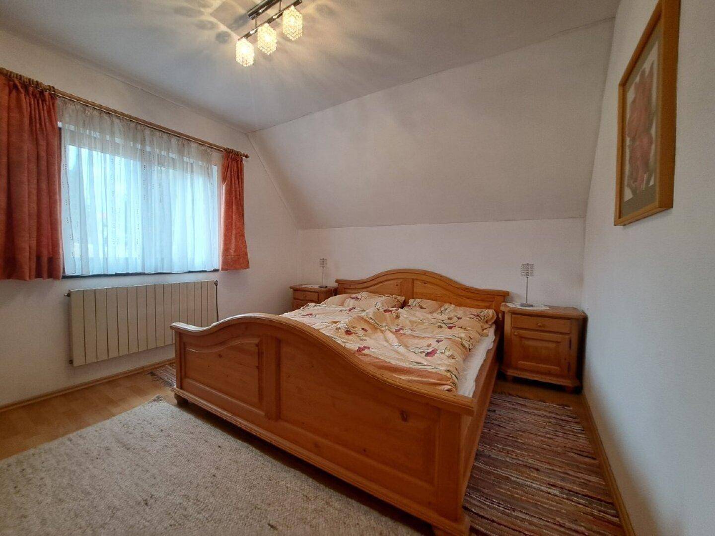 Gemütliches Schlafzimmer mit Holzbett, Teppich und Dachschräge, gut beleuchtet.