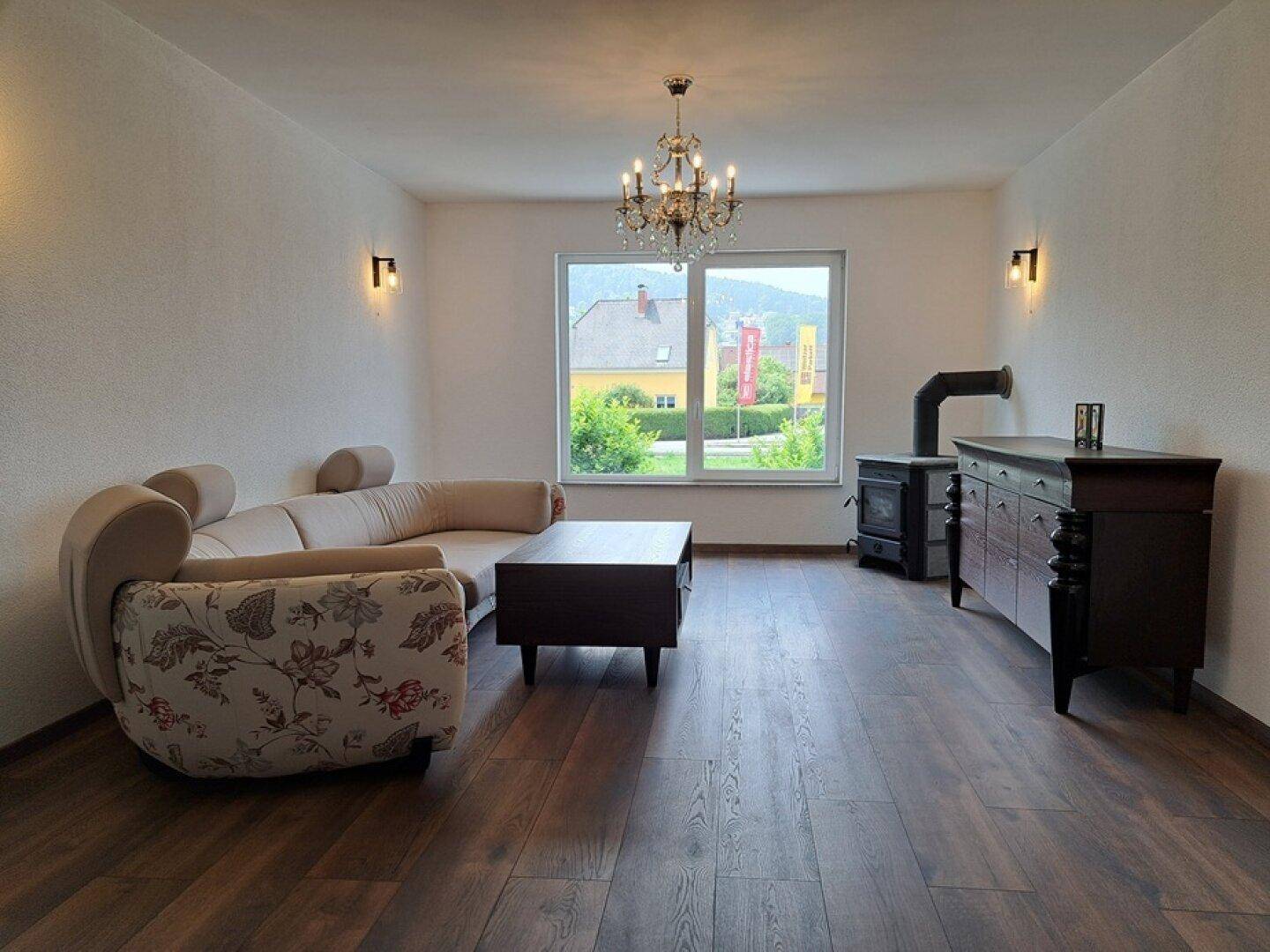 Gemütliches Wohnzimmer mit Holzboden, Kaminofen und Blick ins Grüne durch das Fenster.