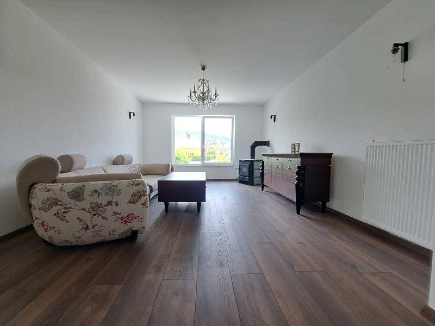 Helles Wohnzimmer mit Holzboden, Heizkörper und elegantem Kronleuchter an der Decke.