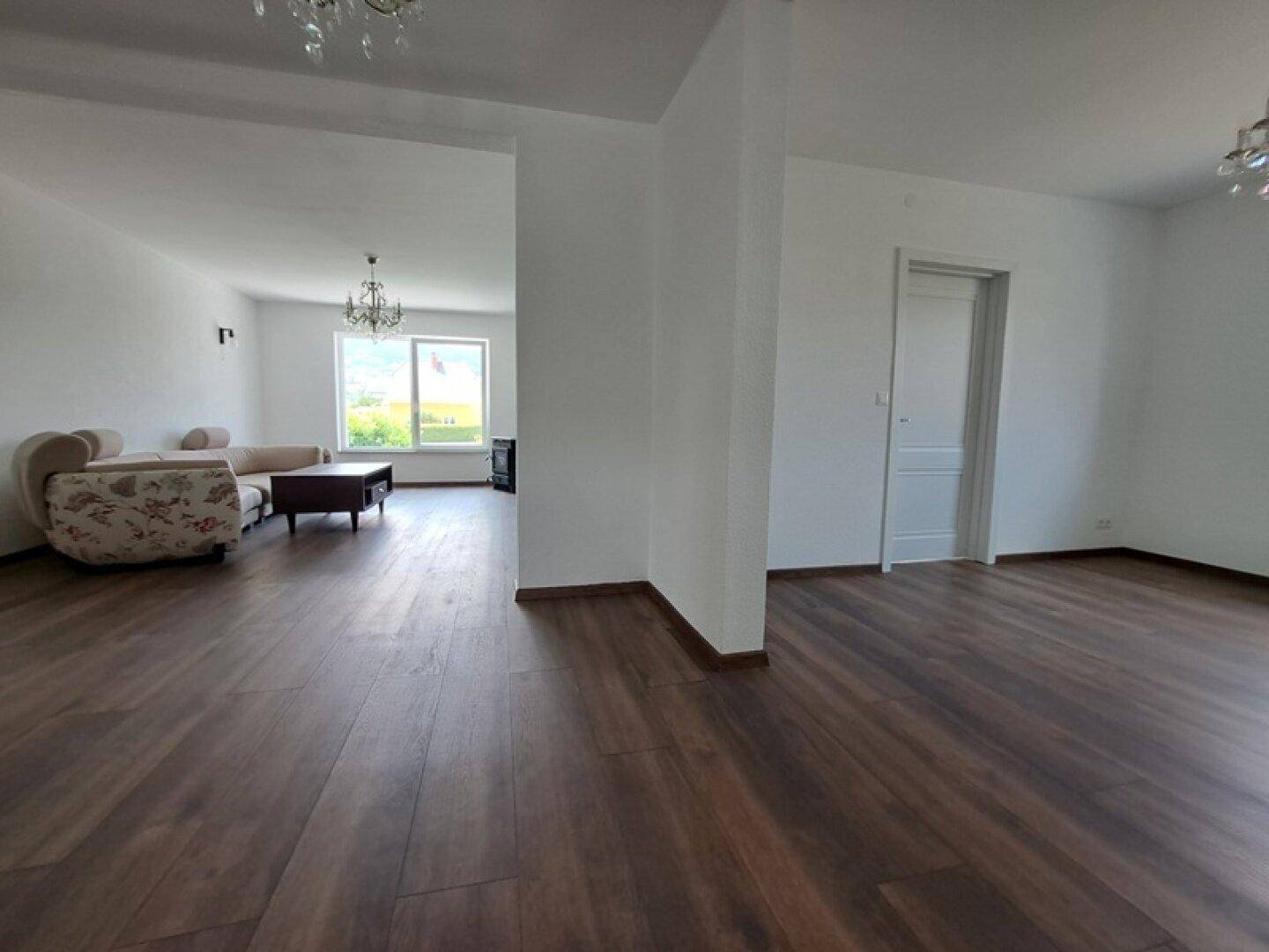 Offener Wohnbereich mit Holzboden und Übergang zu weiteren Räumen, hell und einladend.