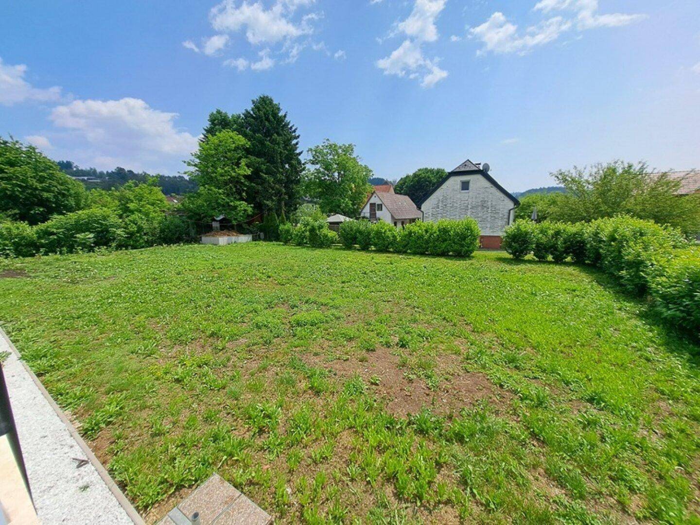 Großer, gepflegter Gartenbereich mit Rasenfläche und Hecken im Hintergrund unter blauem Himmel.