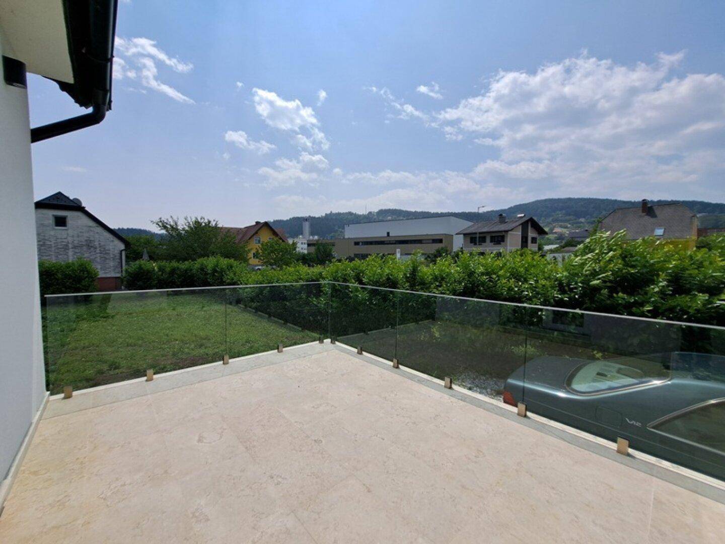 Geräumige Terrasse mit Glasbrüstung und weitem Blick auf die grüne Umgebung und Berge.