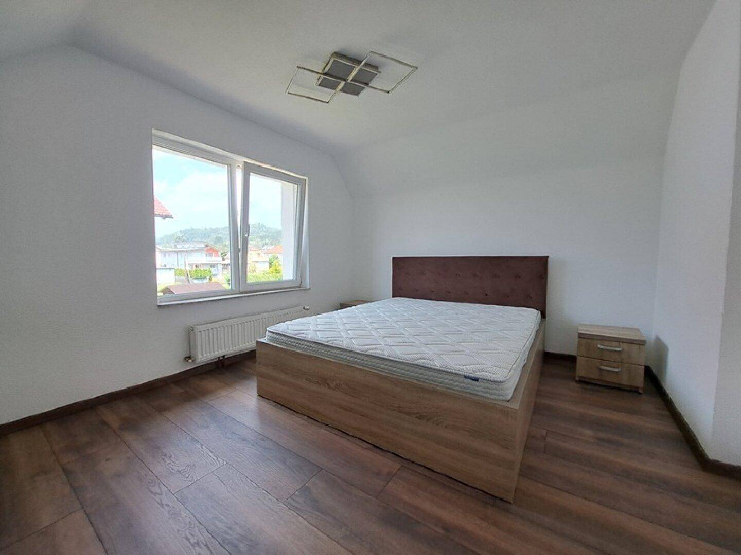 Geräumiges Schlafzimmer mit Holzboden, Doppelbett und großem Fenster für viel Tageslicht.