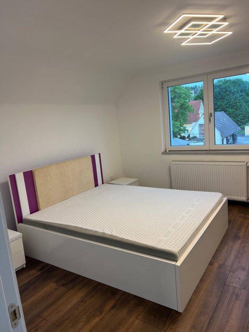 Modernes Schlafzimmer mit Holzboden, Doppelbett und Fenster mit Ausblick in die Umgebung.