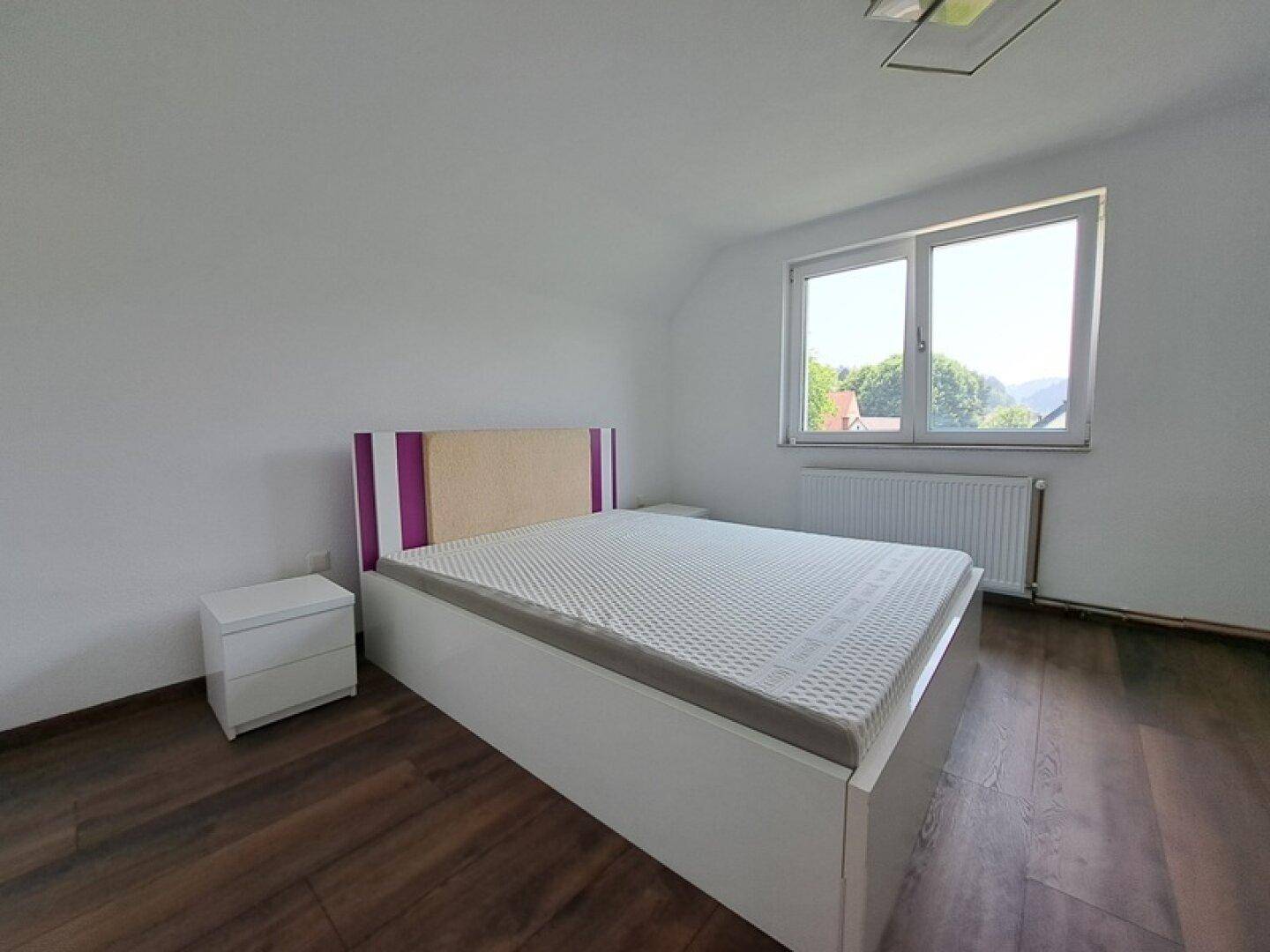 Helles Schlafzimmer mit Holzboden, Doppelbett und Fenster mit Blick ins Grüne.